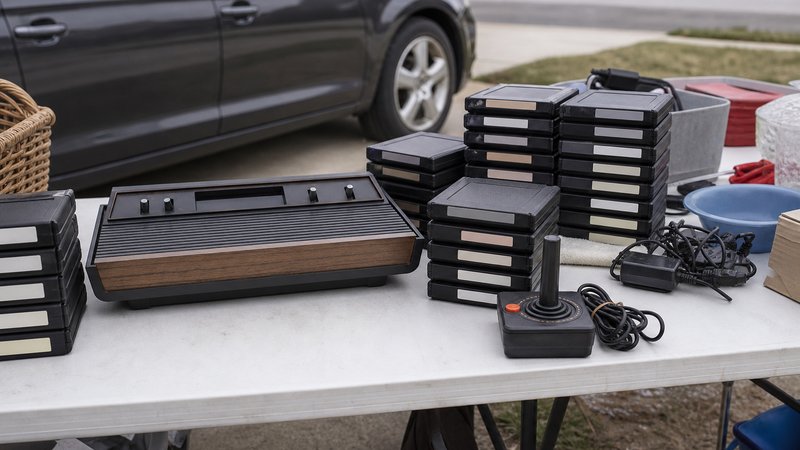 Driveway sale table stacked with Atari 2600 games cartridges beside a woodgrain console