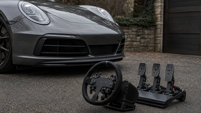 Sim racing wheel and pedals for beginners photographed beside a real car in a driveway